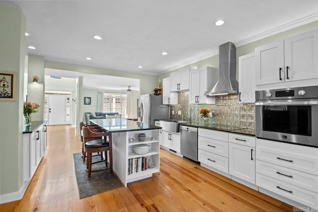 kitchen with white cabinetry, sink, stainless steel appliances, and wall chimney range hood