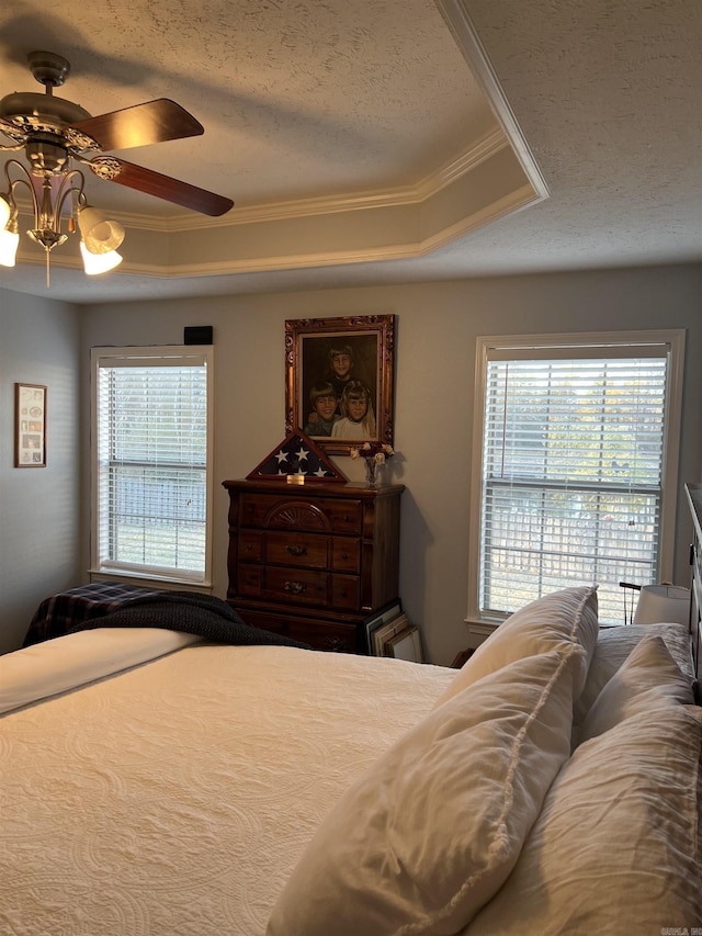 bedroom featuring a textured ceiling, ceiling fan, a raised ceiling, and crown molding