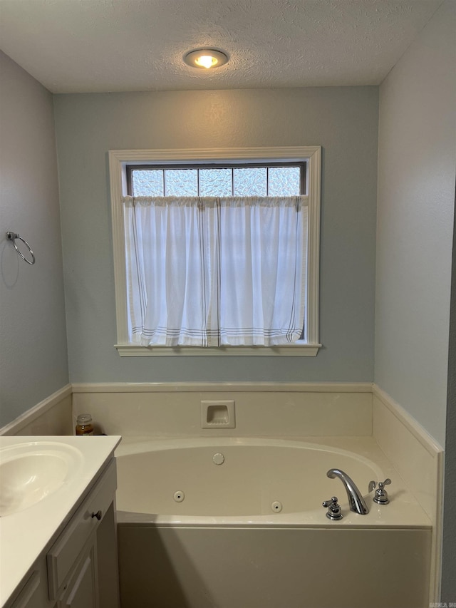 bathroom with vanity, a textured ceiling, a tub, and a healthy amount of sunlight