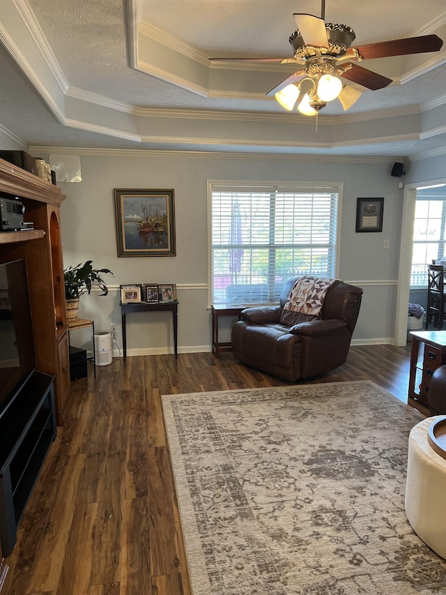 living room with ceiling fan, a raised ceiling, crown molding, and dark wood-type flooring