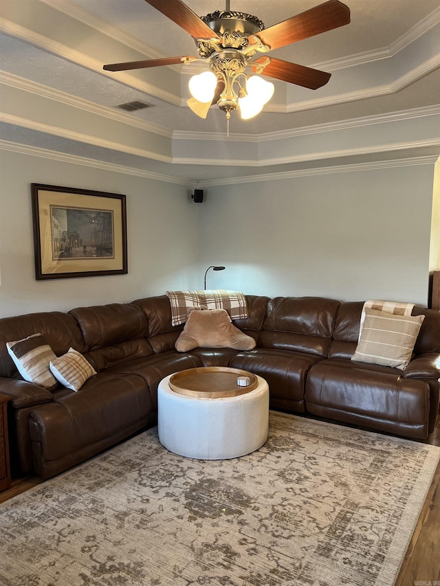 living room featuring hardwood / wood-style flooring, ceiling fan, a raised ceiling, and ornamental molding