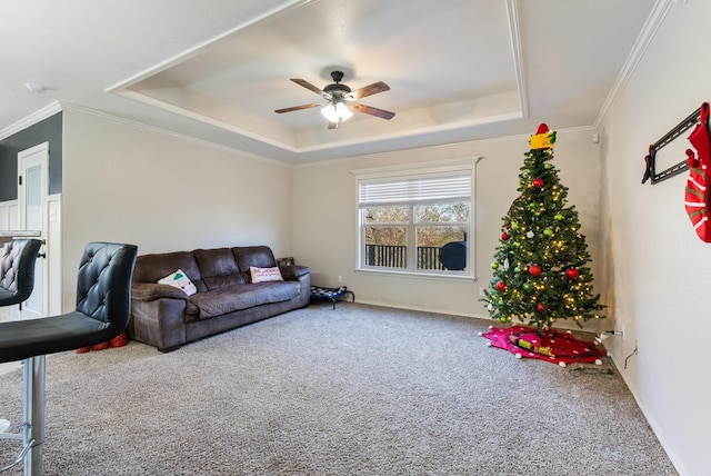 carpeted living room with a raised ceiling, ceiling fan, and crown molding