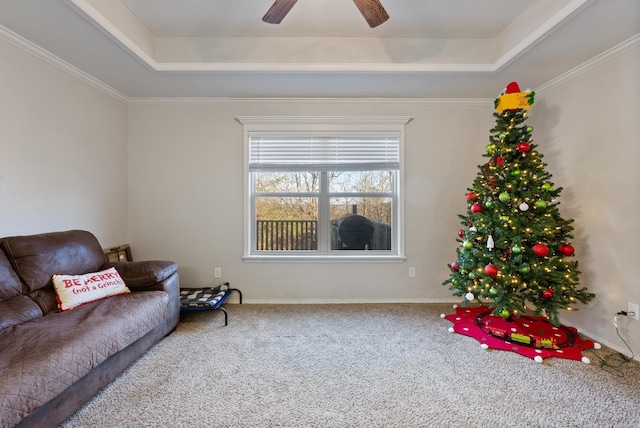 living area with a raised ceiling, crown molding, carpet, and ceiling fan