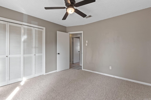 unfurnished bedroom with ceiling fan, a closet, light colored carpet, and a textured ceiling