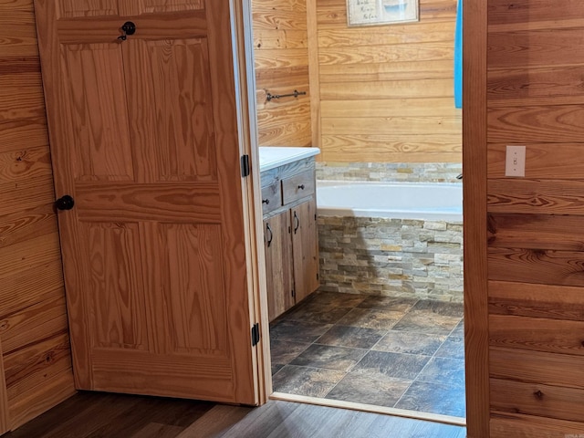 bathroom featuring vanity, wood walls, wood-type flooring, and a bath