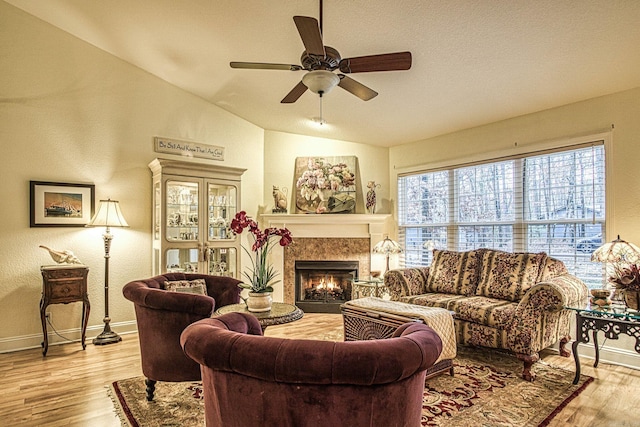 living room with ceiling fan, light hardwood / wood-style flooring, a textured ceiling, lofted ceiling, and a fireplace