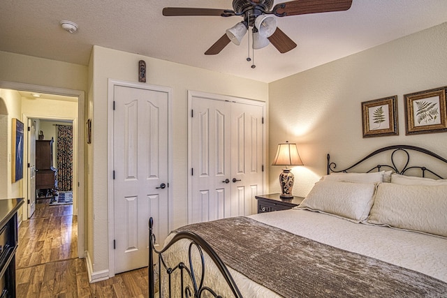 bedroom featuring multiple closets, ceiling fan, a textured ceiling, and hardwood / wood-style flooring