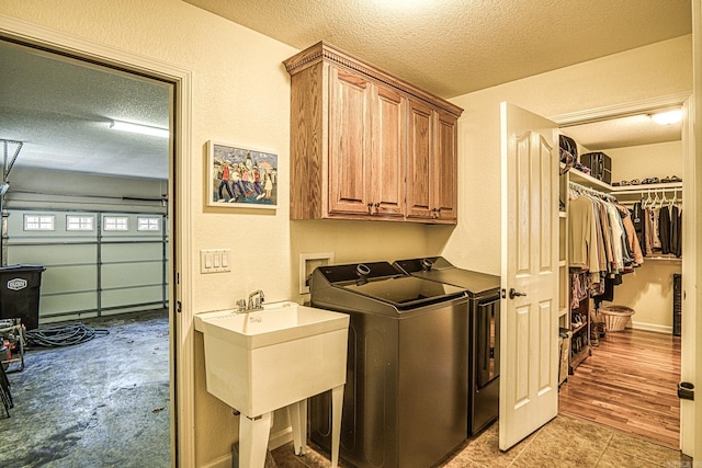 laundry area with sink, cabinets, a textured ceiling, washer and dryer, and light wood-type flooring