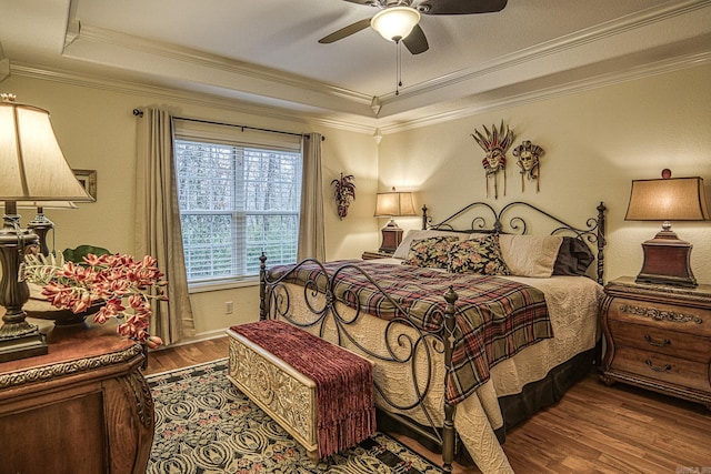 bedroom with hardwood / wood-style flooring, ceiling fan, ornamental molding, and a tray ceiling