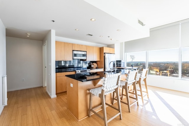 kitchen with a center island, a breakfast bar area, decorative backsplash, light wood-type flooring, and stainless steel appliances