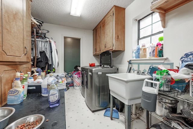 clothes washing area with washer and clothes dryer, sink, cabinets, and a textured ceiling