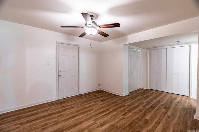 unfurnished bedroom featuring ceiling fan, dark hardwood / wood-style flooring, and two closets