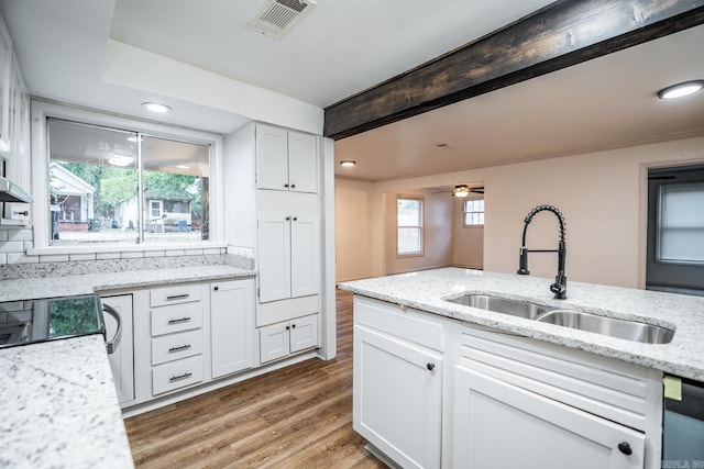 kitchen with light stone countertops, sink, white cabinets, and wood-type flooring