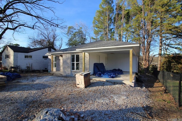 rear view of property with gravel driveway, brick siding, and fence