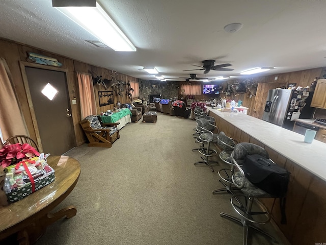 interior space with ceiling fan, stainless steel refrigerator with ice dispenser, a textured ceiling, and wooden walls