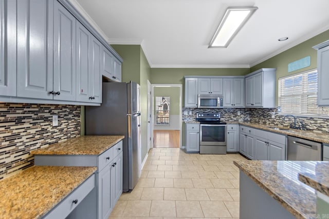 kitchen with appliances with stainless steel finishes, ornamental molding, gray cabinetry, and sink