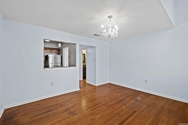 empty room featuring dark wood-type flooring and an inviting chandelier