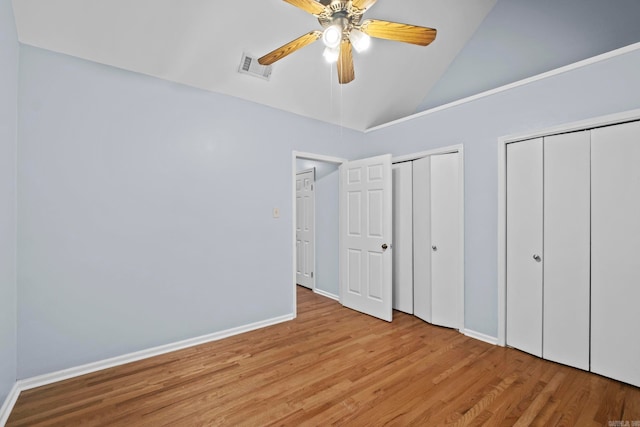 unfurnished bedroom featuring ceiling fan, multiple closets, high vaulted ceiling, and light hardwood / wood-style flooring