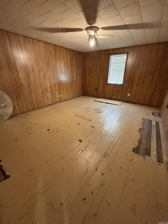 unfurnished room featuring hardwood / wood-style floors, ceiling fan, and wooden walls