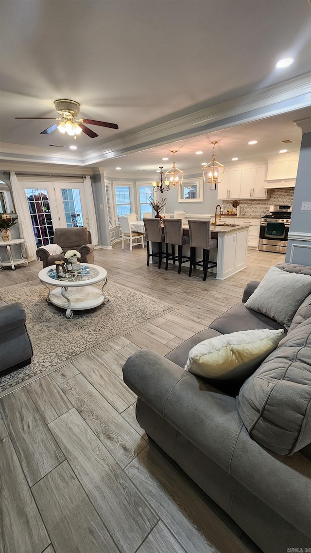 living room with sink, ornamental molding, ceiling fan with notable chandelier, and light wood-type flooring