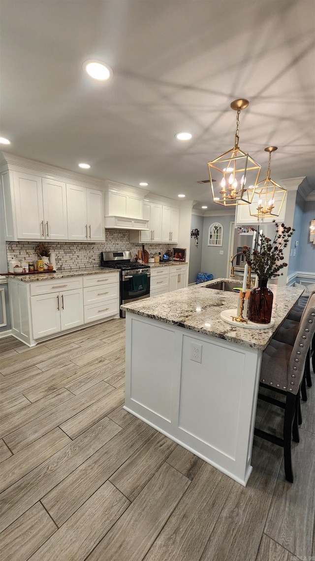 kitchen with white cabinetry, an island with sink, light wood-type flooring, and stainless steel range with gas stovetop