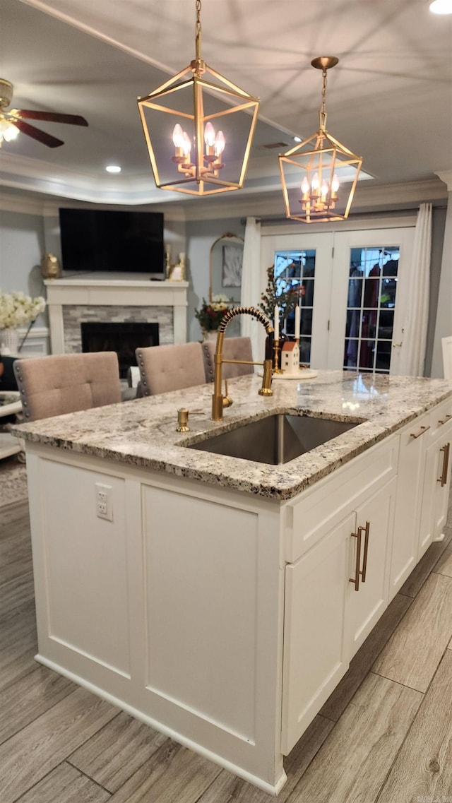 kitchen with pendant lighting, sink, light wood-type flooring, light stone counters, and white cabinetry