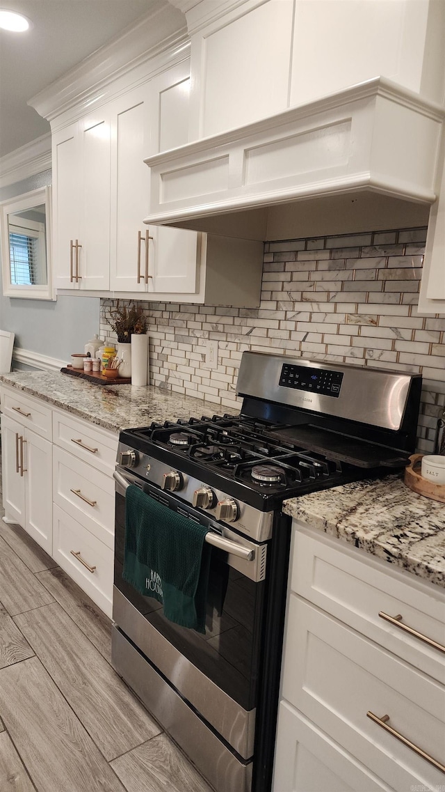 kitchen featuring light stone countertops, tasteful backsplash, ornamental molding, stainless steel range with gas cooktop, and white cabinetry