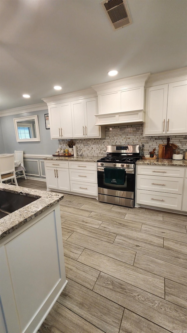 kitchen featuring light stone counters, ornamental molding, white cabinets, light hardwood / wood-style floors, and stainless steel range with gas stovetop