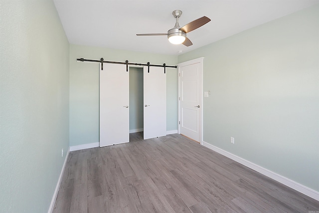 unfurnished bedroom featuring ceiling fan, light hardwood / wood-style floors, a barn door, and a closet