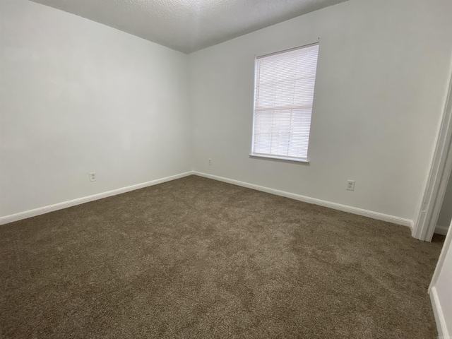 unfurnished room with dark carpet and a textured ceiling