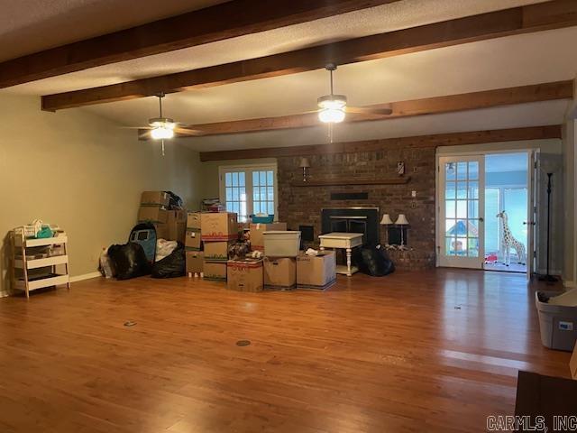 living room with ceiling fan, a brick fireplace, beam ceiling, and wood-type flooring