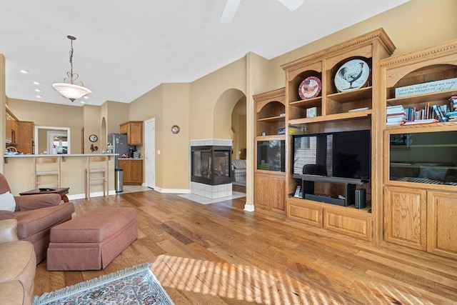 living room with a tile fireplace, ceiling fan, and light wood-type flooring