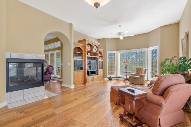 living room featuring ceiling fan, a fireplace, a wealth of natural light, and light hardwood / wood-style flooring