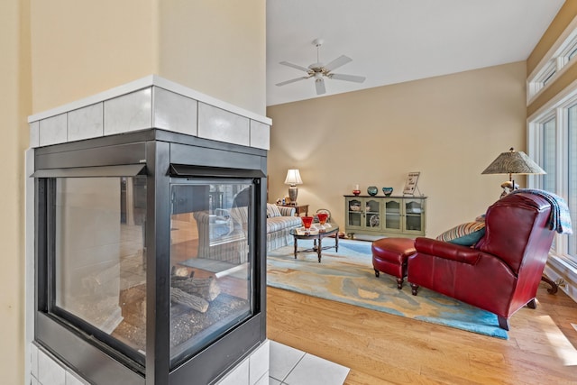 living room with ceiling fan, a tiled fireplace, a high ceiling, and light hardwood / wood-style flooring