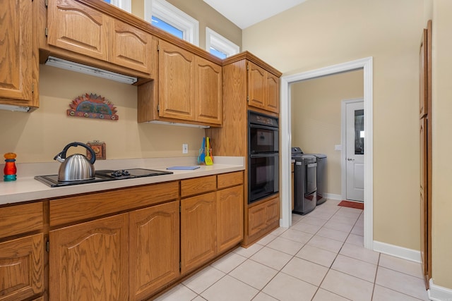 kitchen featuring stovetop, light tile patterned floors, black double oven, and washer and clothes dryer