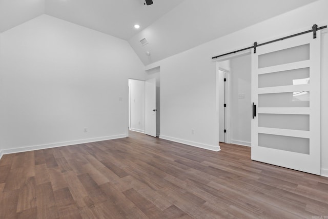 unfurnished bedroom with lofted ceiling, hardwood / wood-style floors, and a barn door