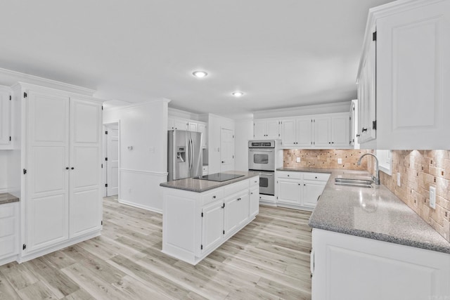 kitchen with light wood-type flooring, stainless steel appliances, a kitchen island, sink, and white cabinetry