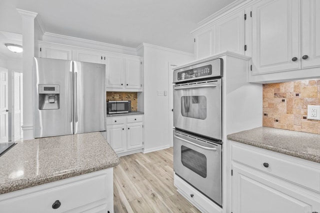 kitchen featuring white cabinets, decorative backsplash, appliances with stainless steel finishes, and light hardwood / wood-style flooring