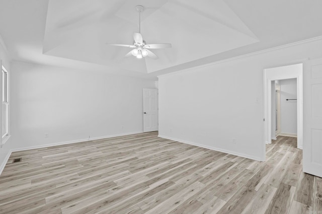 spare room with a tray ceiling, ceiling fan, ornamental molding, and light wood-type flooring