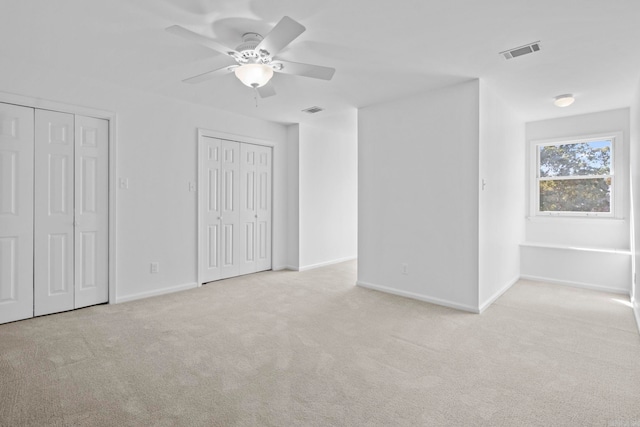 unfurnished bedroom featuring light carpet, two closets, and ceiling fan