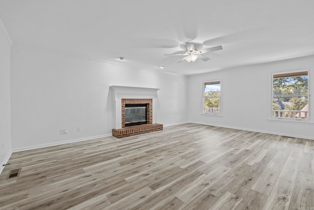 unfurnished living room featuring a healthy amount of sunlight, light hardwood / wood-style floors, ornamental molding, and a brick fireplace