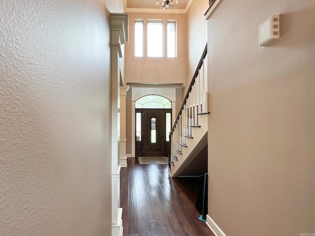 entryway with an inviting chandelier, dark wood-type flooring, and ornamental molding