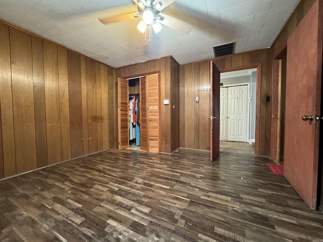 unfurnished room featuring wooden walls, ceiling fan, and dark wood-type flooring