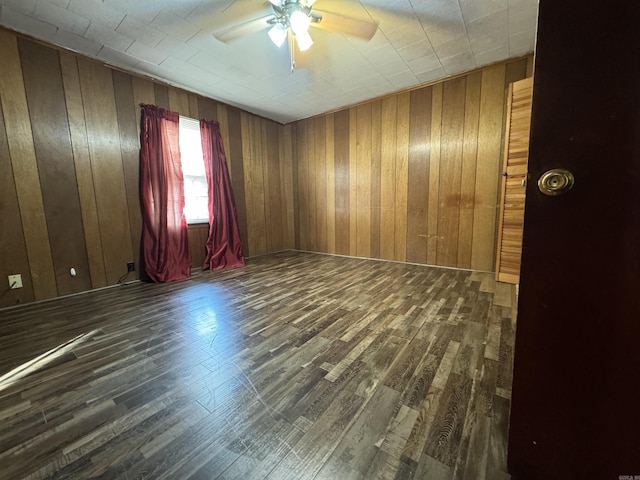 unfurnished room featuring wood walls, dark hardwood / wood-style flooring, and ceiling fan