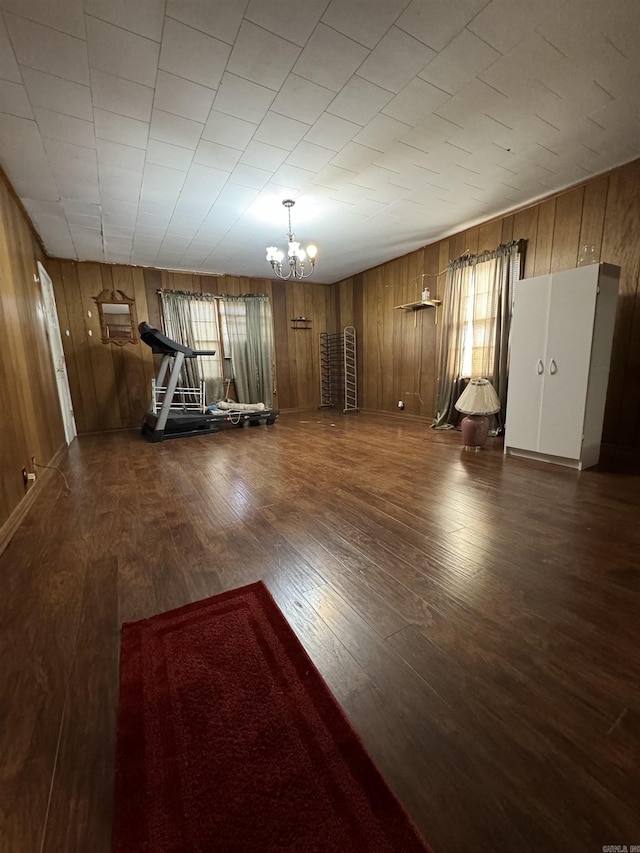 exercise area featuring wood walls, dark wood-type flooring, and an inviting chandelier