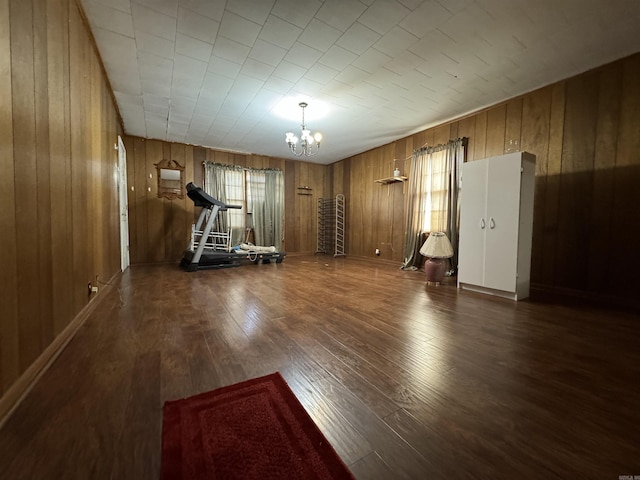 exercise room featuring wooden walls, dark wood-type flooring, and an inviting chandelier