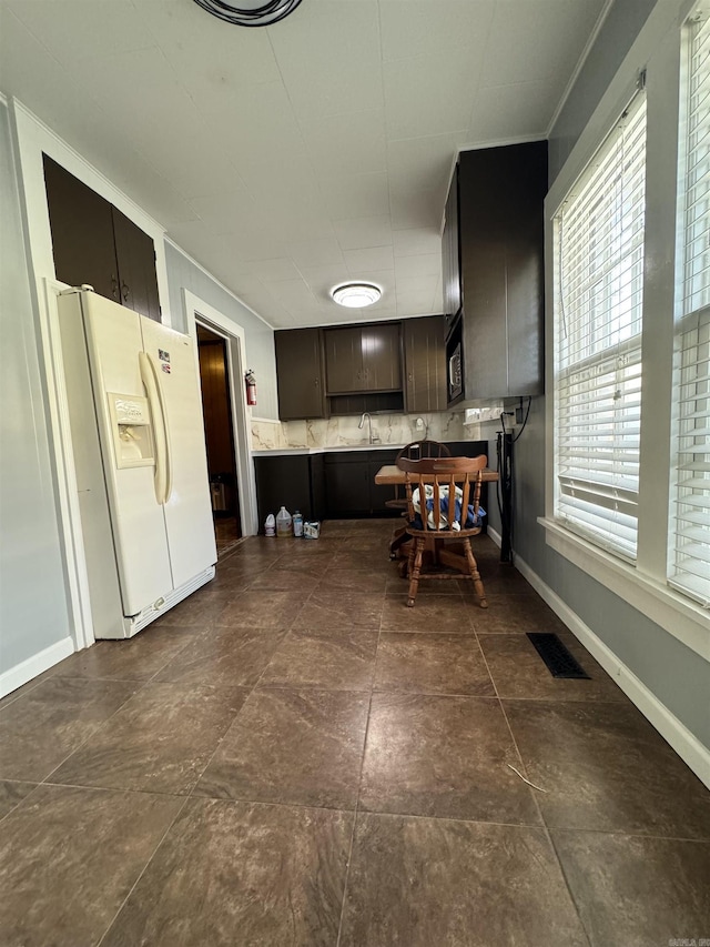 kitchen with backsplash, dark brown cabinets, crown molding, sink, and white refrigerator with ice dispenser