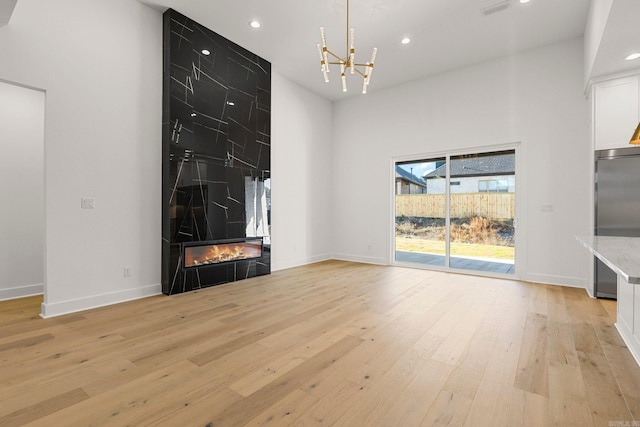 unfurnished living room with a tiled fireplace, a chandelier, light hardwood / wood-style floors, and a high ceiling