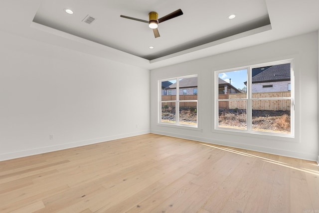 spare room featuring a tray ceiling, ceiling fan, and light hardwood / wood-style flooring