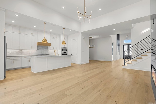 kitchen featuring a towering ceiling, a kitchen island with sink, light hardwood / wood-style floors, white cabinetry, and hanging light fixtures